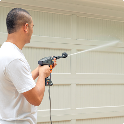 Persona usando la hidrolavadora portátil Inbogo para limpiar exteriores.